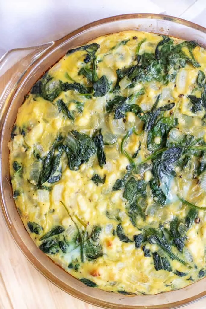 Crustless spinach feta quiche slice on a plate with fresh herbs